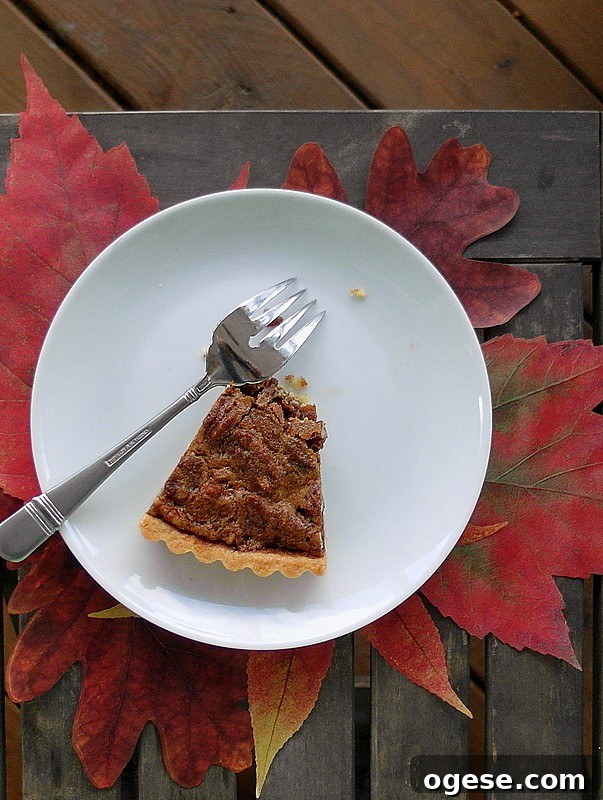 Coffee pecan tart delivers all the flavor you want from a pecan pie but in a slimmer package. The coffee flavor really supports the pecan flavor. A slice of coffee pecan tart on a plate with fall leaves under it.