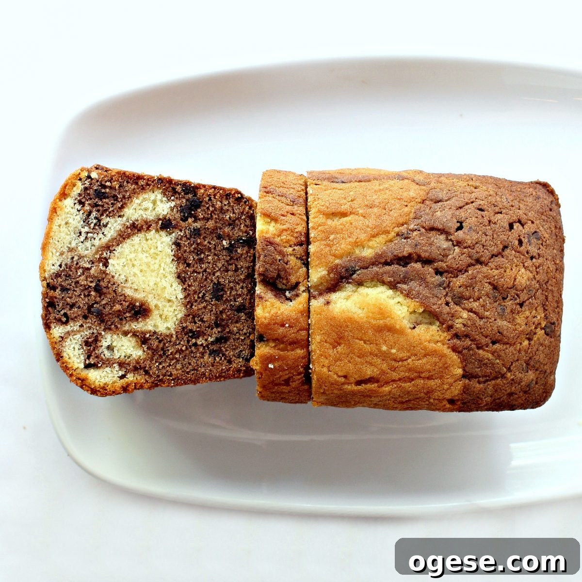 Moist Chocolate Marble Pound Cake Recipe 6 Marbled loaf on a white platter with one cut slice showing the marbled pattern inside.