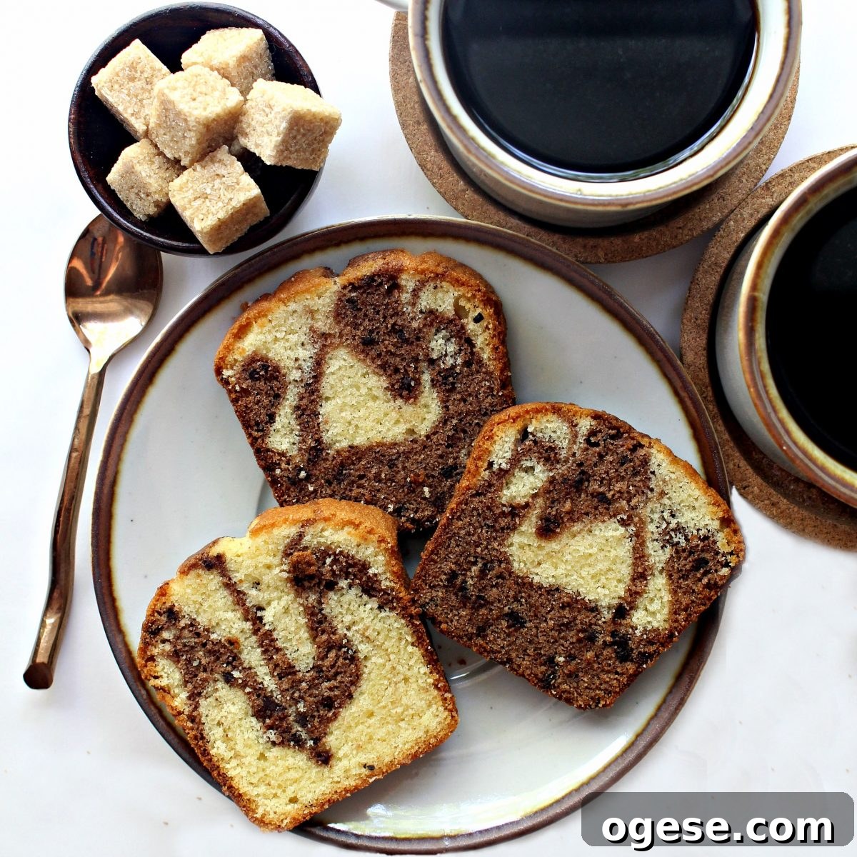 Moist Chocolate Marble Pound Cake Recipe 7 Three slices of marbled cake on a plate next to two cups of coffee.