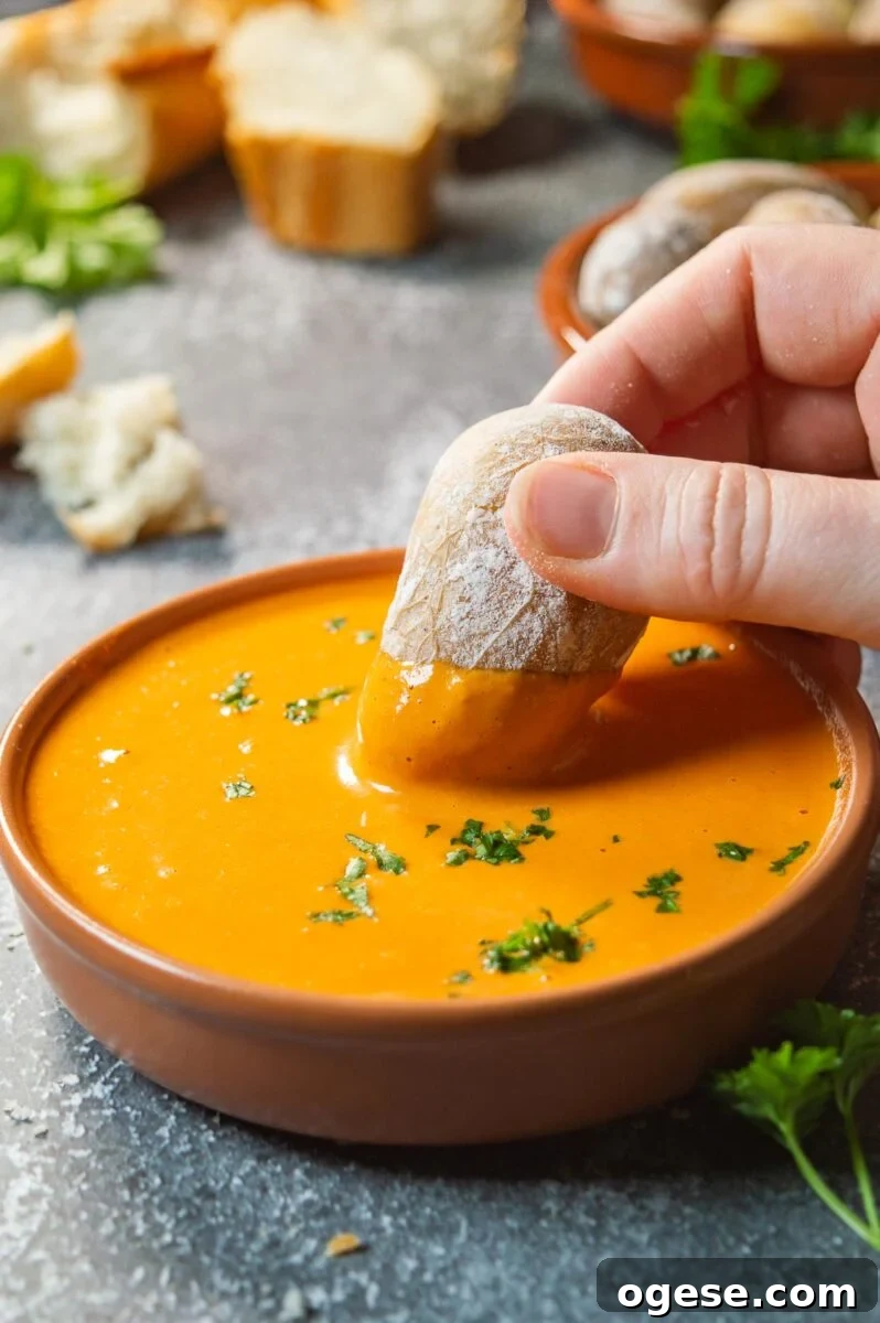 A hand dipping a potato into a dish with orange sauce.