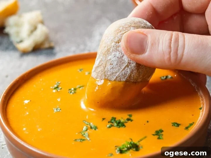 A hand dipping a potato into a dish with orange sauce.