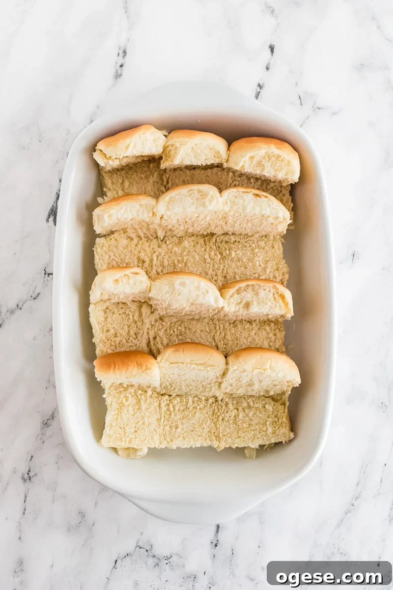 Ultimate Cheesy Ham and Melted Cheese Sliders Recipe 6 Sliced Kings Hawaiian rolls placed in baking dish.