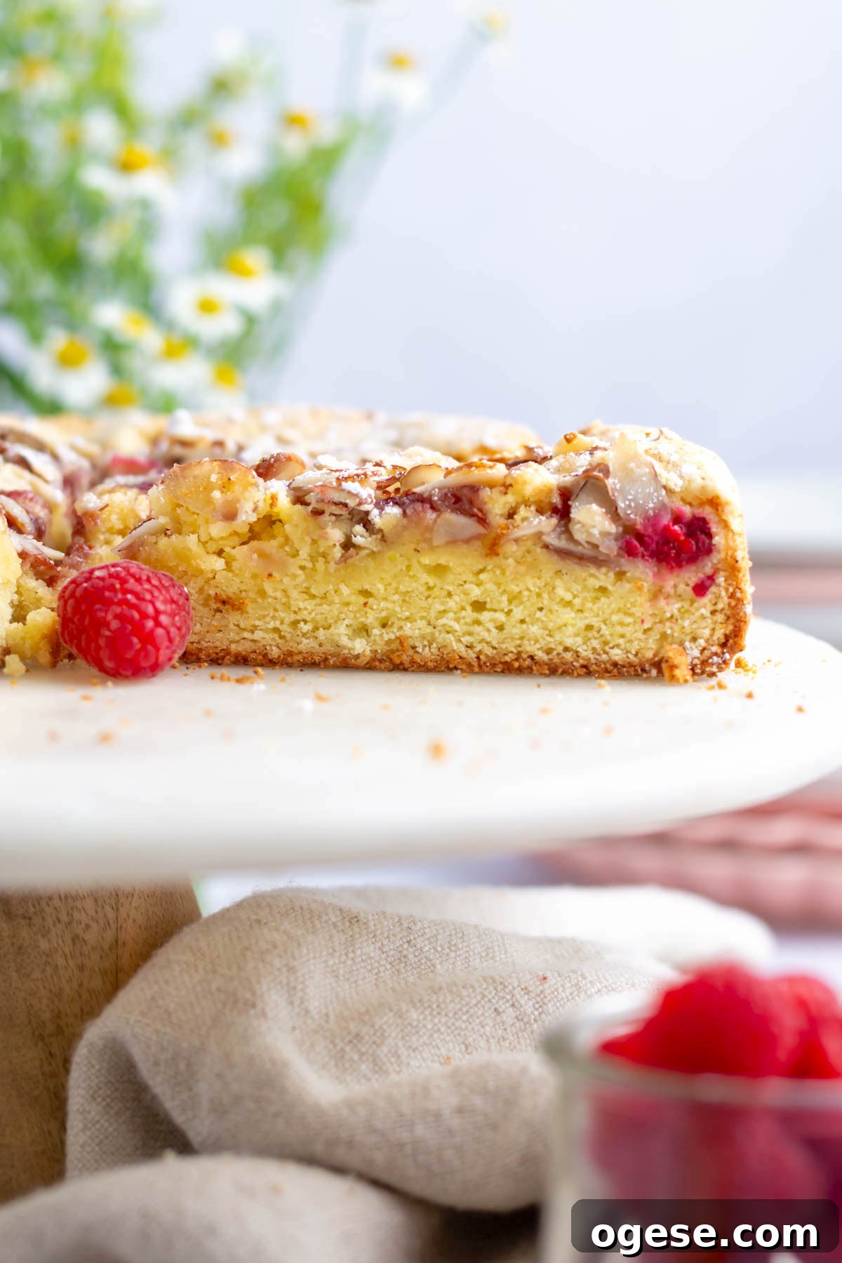 sliced cake on a cake stand with fresh raspberries and flowers in the background