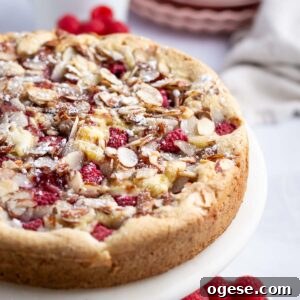 raspberry almond cake on a cake stand with plates in the background