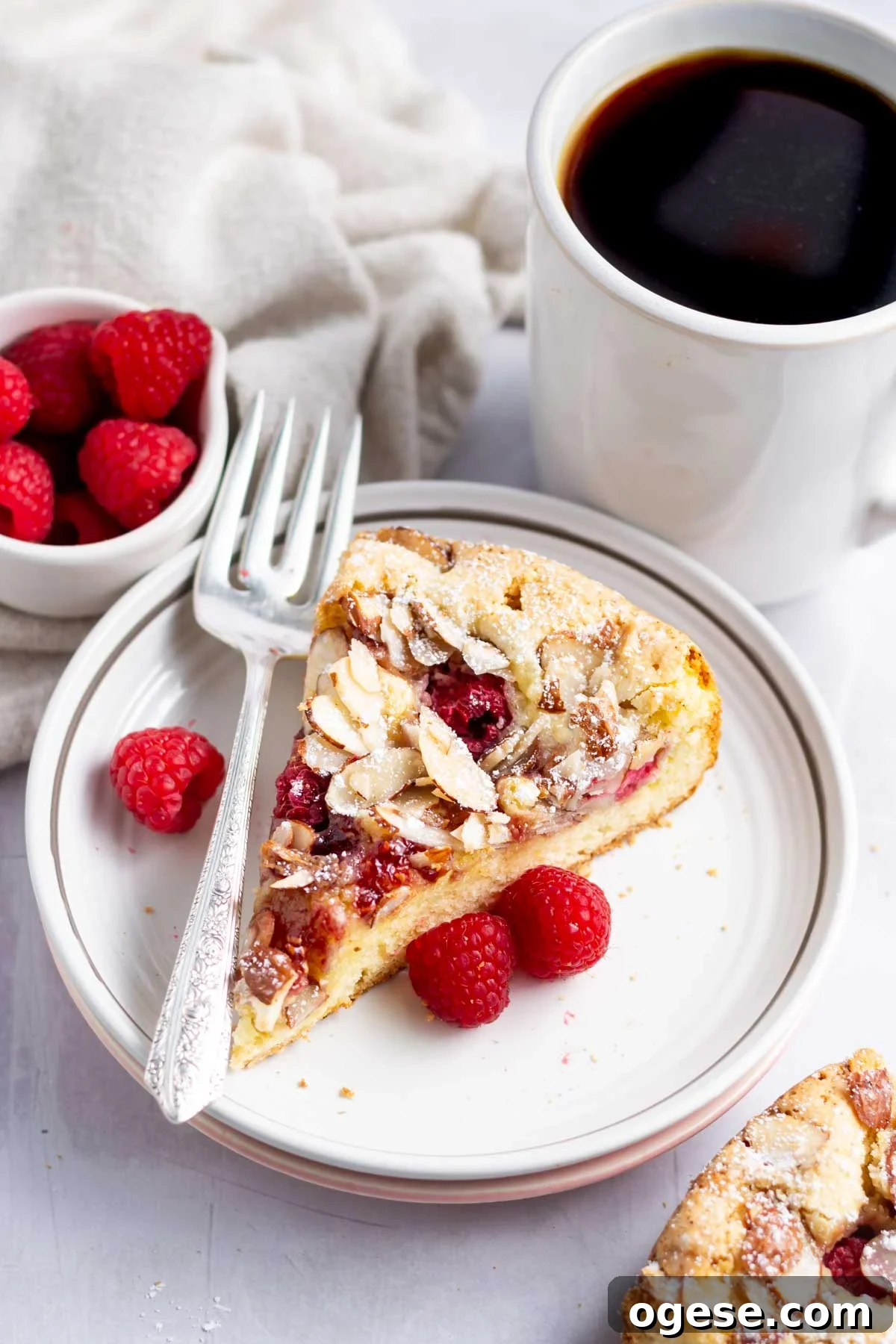 slice of raspberry almond cake on a plate with a fork and a cup of coffee
