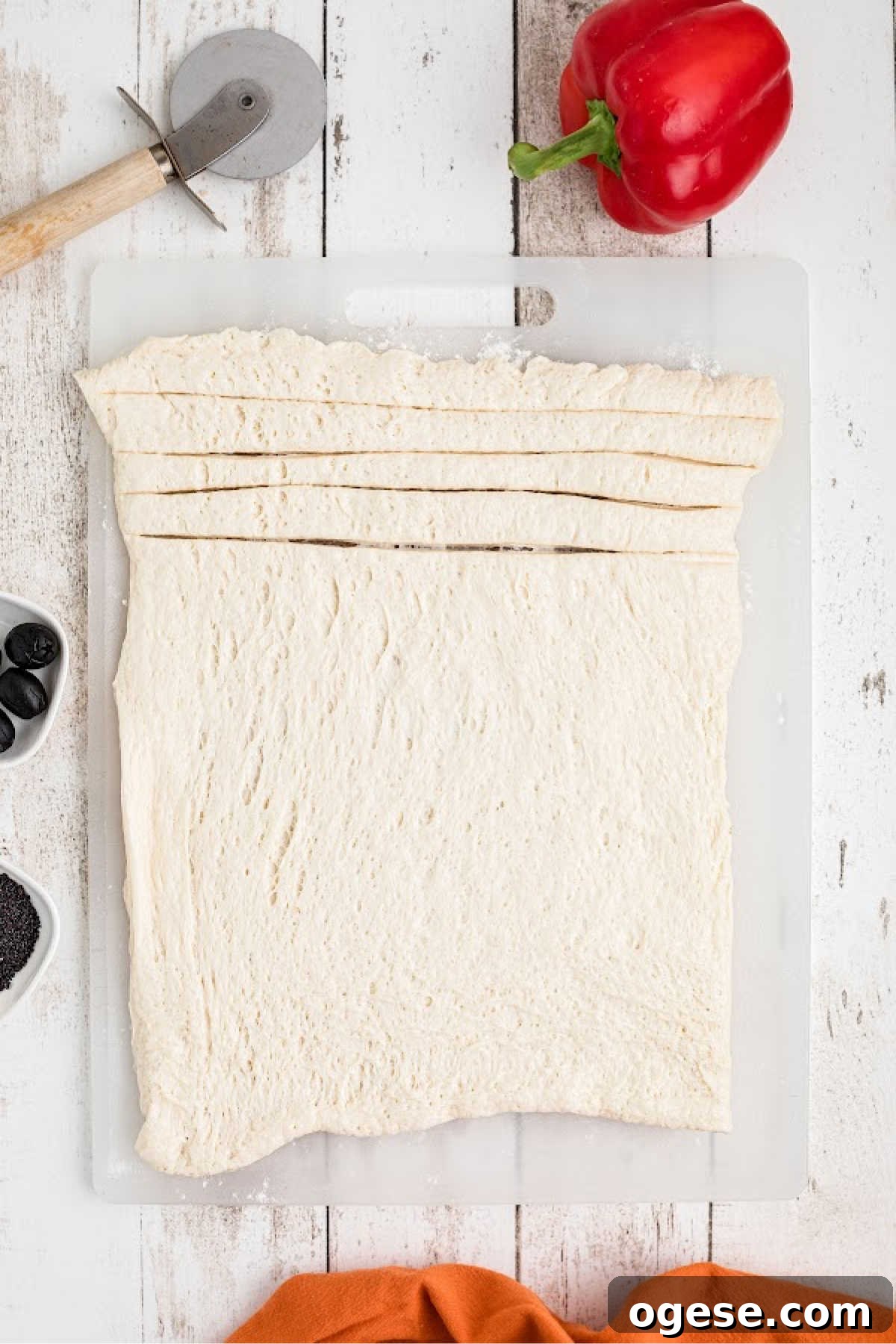 Crispy Breadstick Rattlers: Spicy Sausage-Stuffed Appetizers 4 A sheet of pizza dough being cut with a pizza wheel.