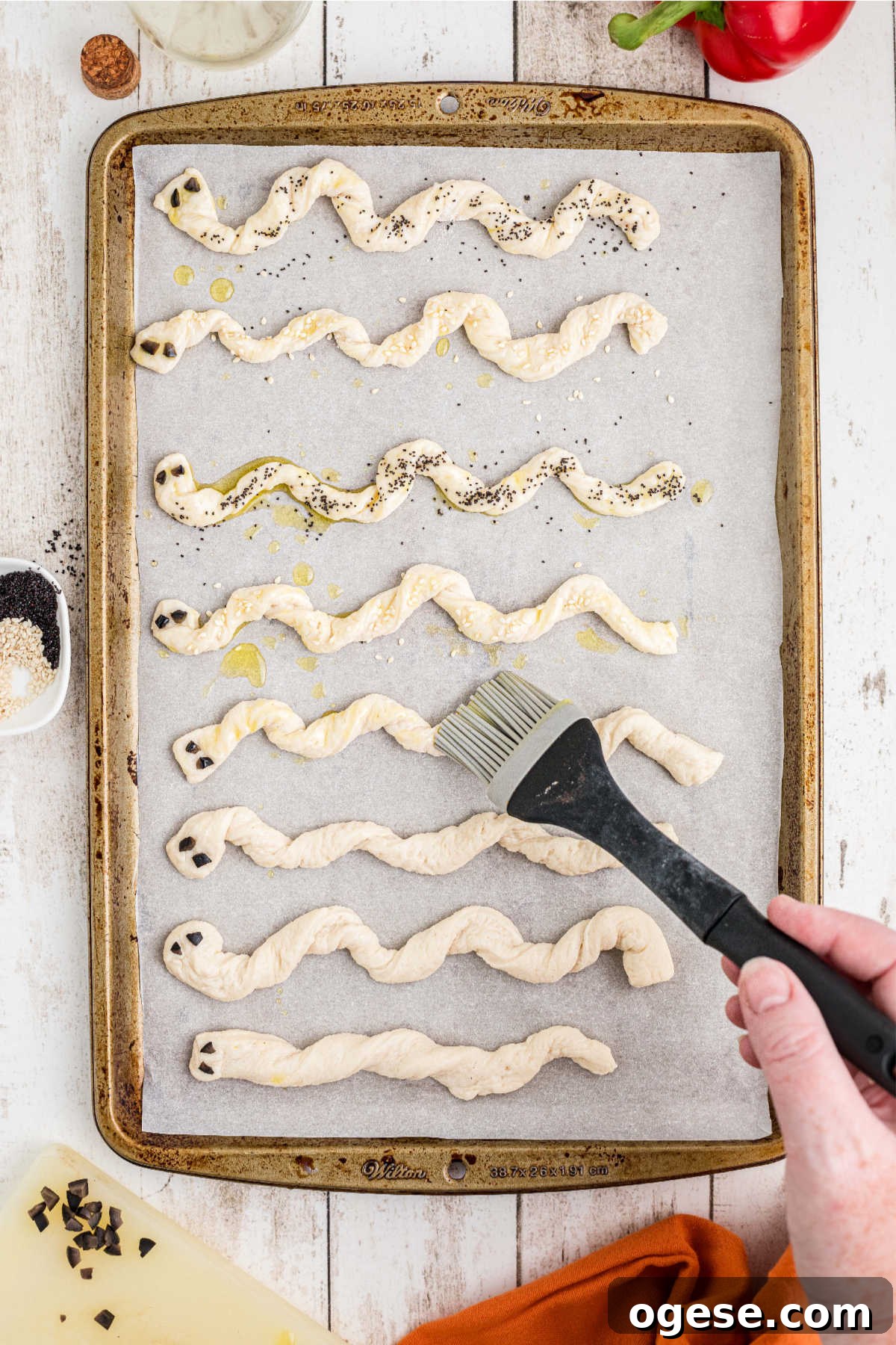 Crispy Breadstick Rattlers: Spicy Sausage-Stuffed Appetizers 6 A pastry brush brushing oil onto strands of pizza dough.