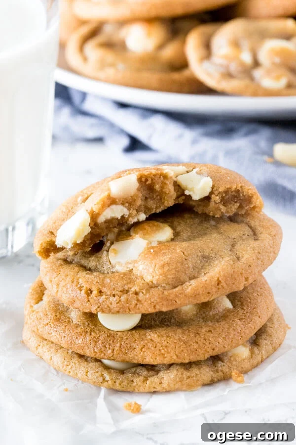 A stack of soft, chewy white chocolate macadamia cookies with the top cookie broken in half to show the chewy center.