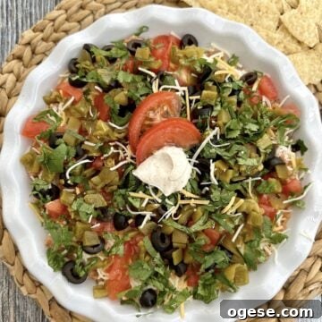 Five layered taco dip in a serving dish on a table with chips.