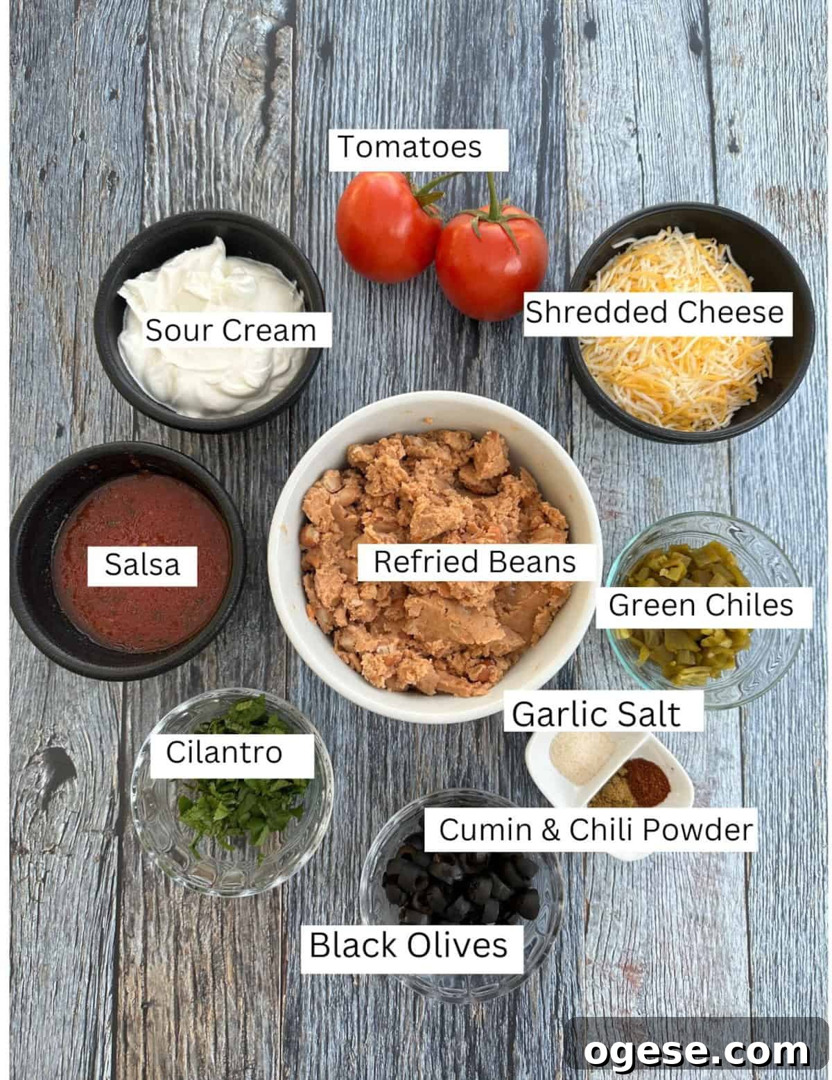 Creamy 5-Layer Bean Dip Recipe for Parties and Game Day 3 Labeled ingredients for five-layer taco dip on a wooden table.