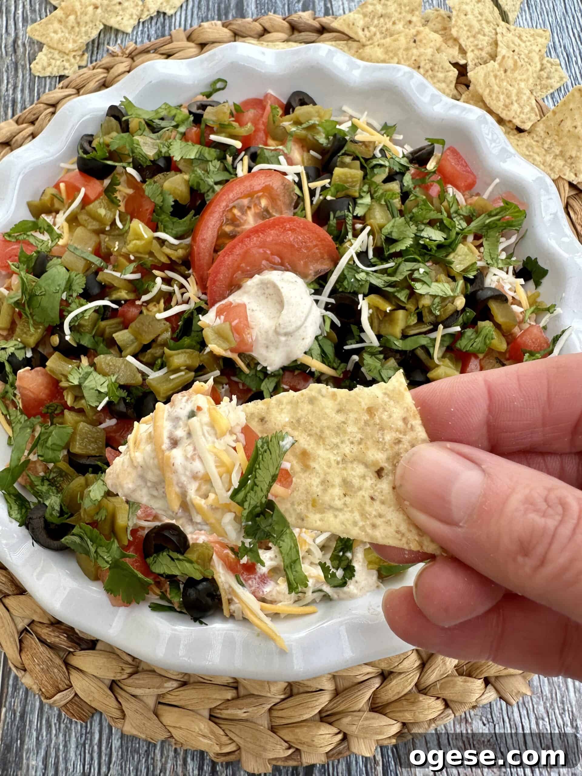Creamy 5-Layer Bean Dip Recipe for Parties and Game Day 5 A hand holding a chip scooping up a serving of taco dip.
