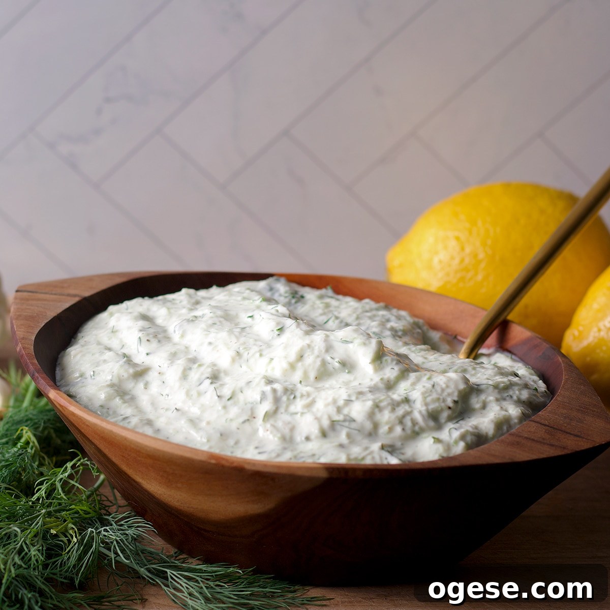 Traditional and Vegan Tzatziki: Two Authentic Recipes You’ll Love 8 A wood bowl filled with tzatziki sauce with fresh dill and lemons on a cutting board next to the bowl.