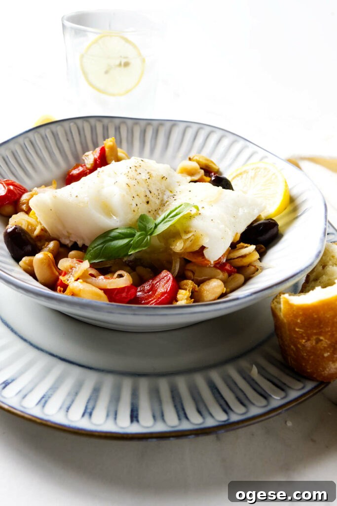 A dish filled with baked cod, beans, and roasted tomatoes.