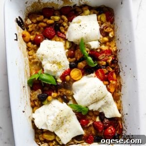 A baking dish filled with roasted cod on tomatoes, beans, and olives.