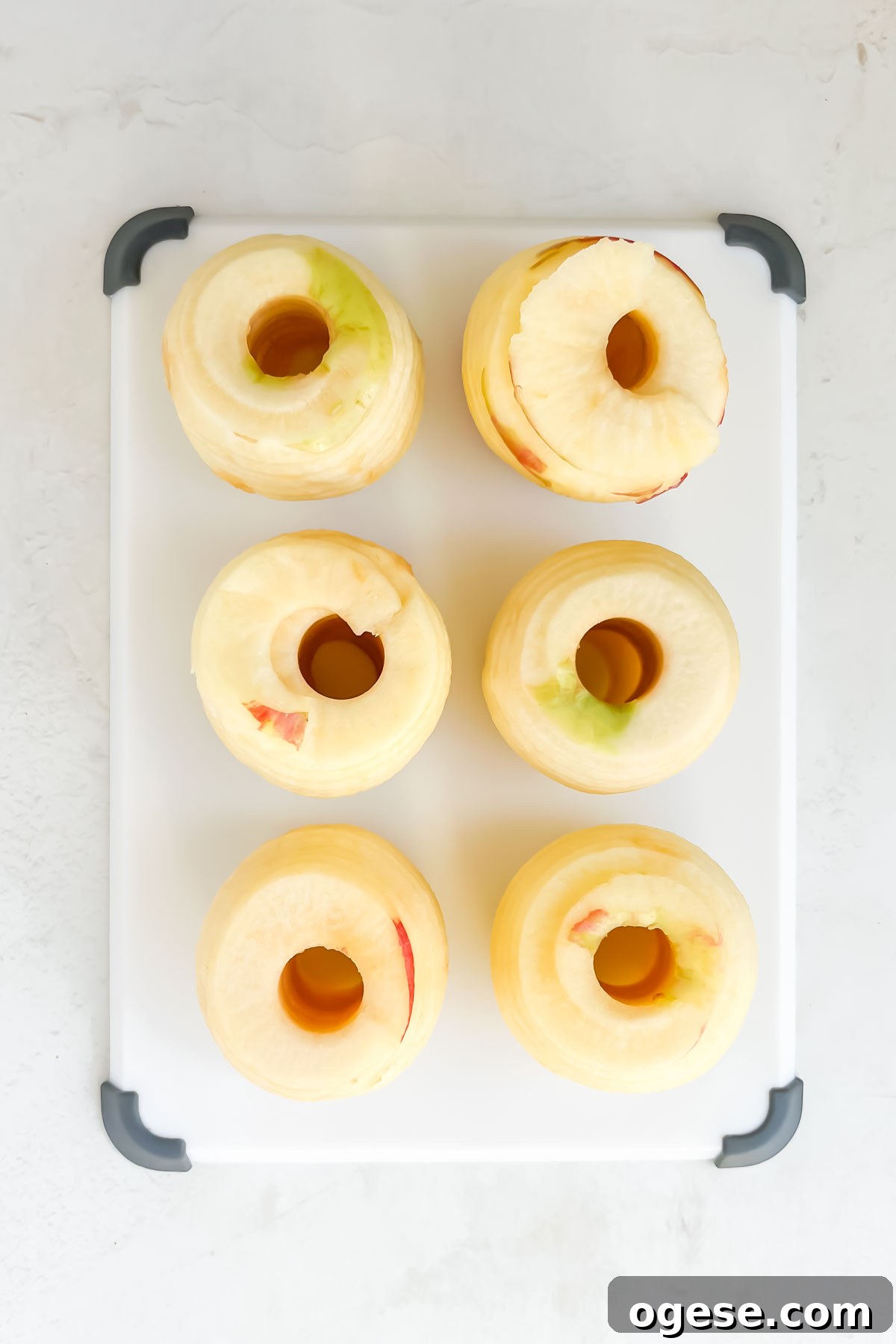 Thin and round apple slices piled on a cutting board on a white backdrop.
