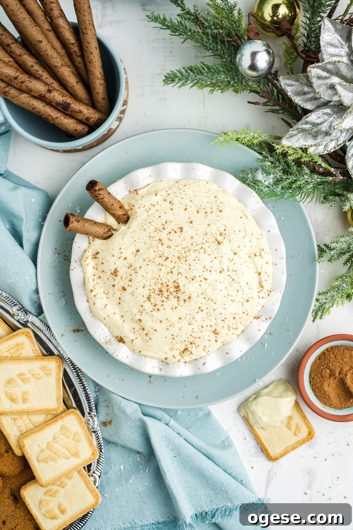 A bowl of eggnog dip on the table on top of a light blue bowl and garnished with cinnamon sticks.