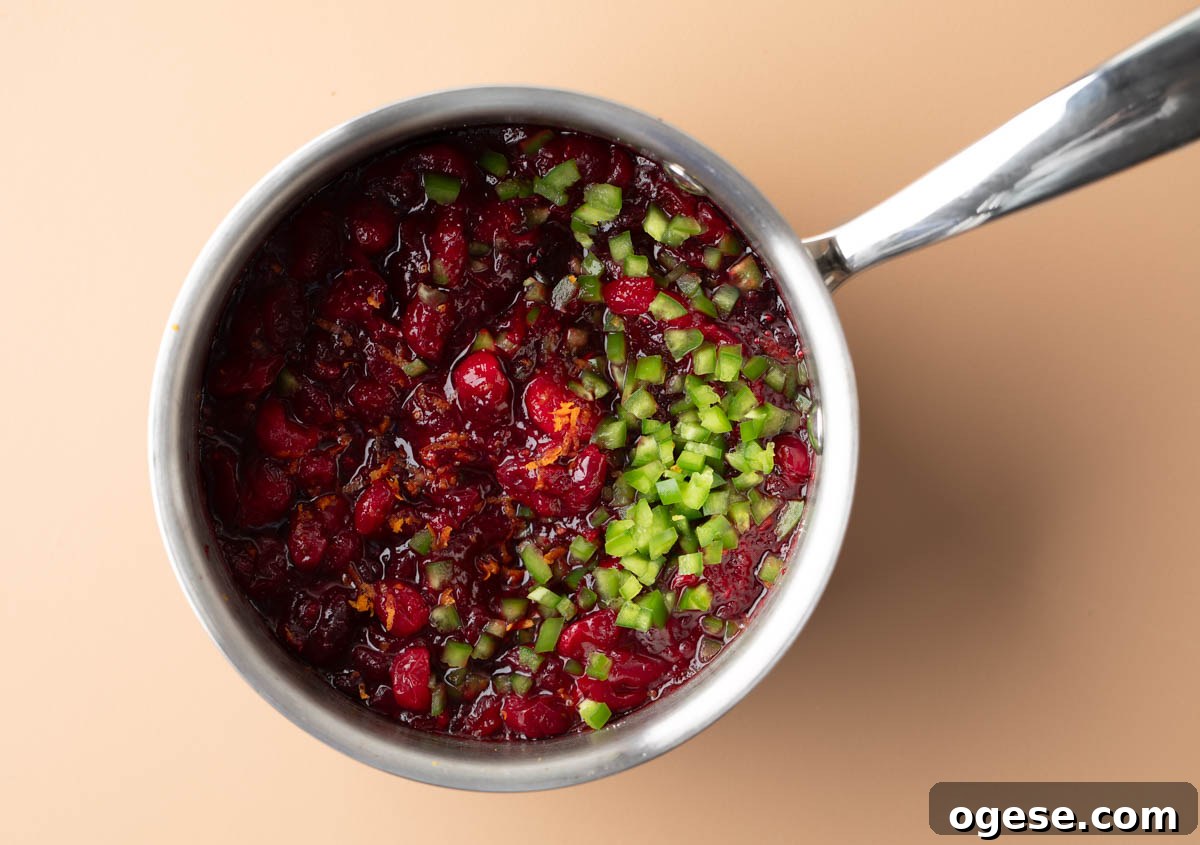 Spicy Jalapeño Cranberry Sauce Recipe for Holiday Meals 5 saucepan with cranberries, orange juice, orange zest, jalapenos, water and sugar simmering