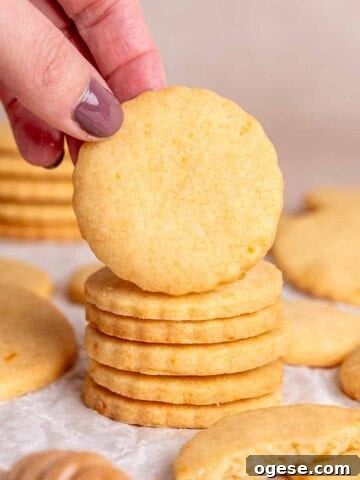 A hand grabbing an orange shortbread cookie from a stack.