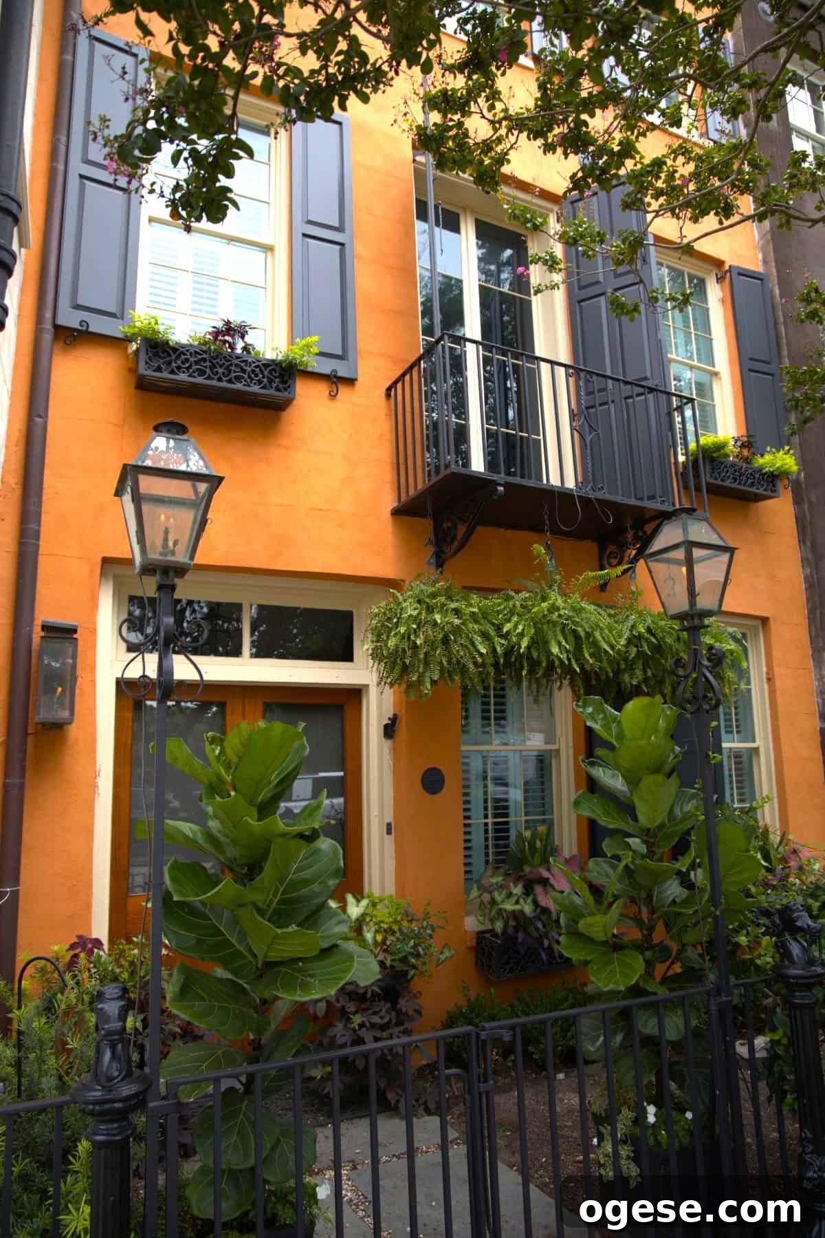 Charleston Travel Guide: Top Attractions, Food & Historic Tours 2 Three-story orange townhouse with black shutters and balcony, window flower boxes, lush greenery, and a black iron fence in front—perfect for any Charleston travel guide.