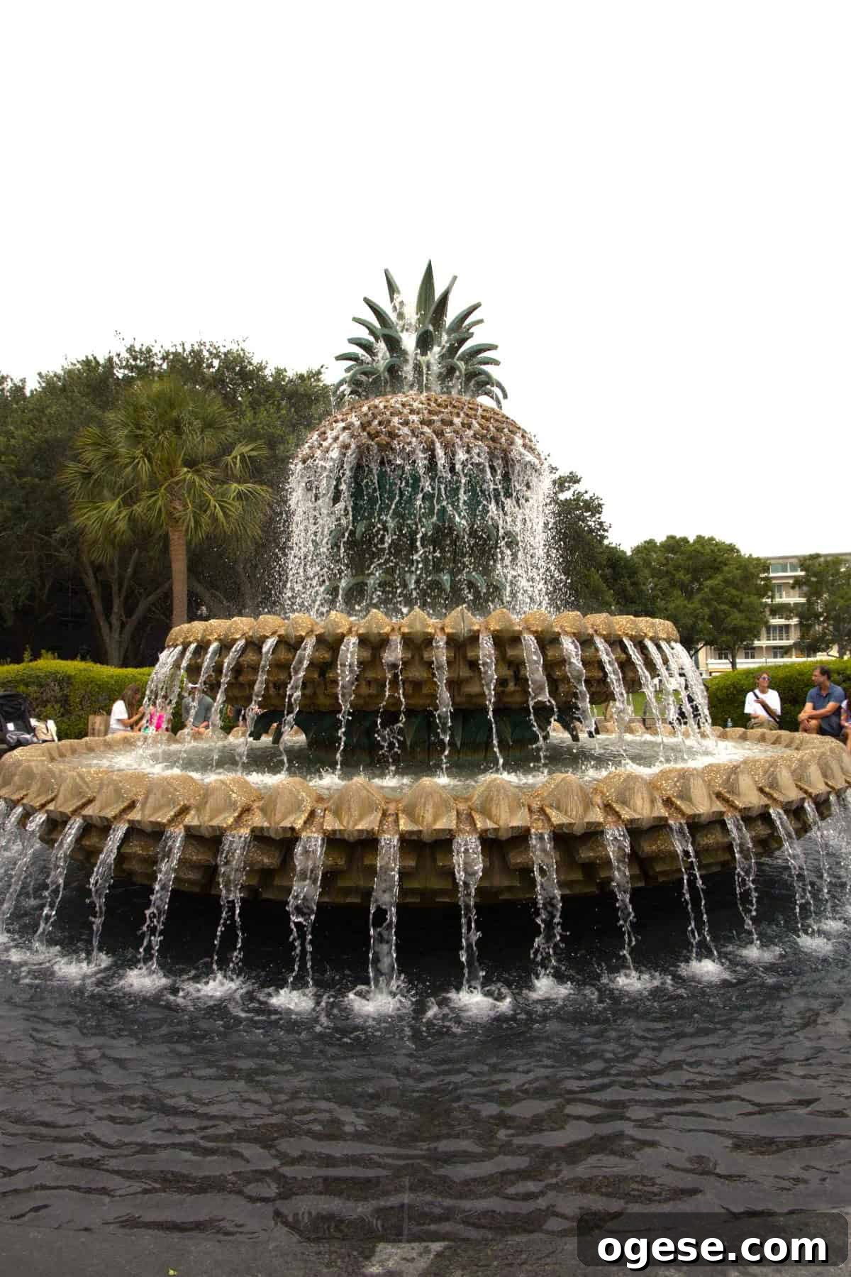 Charleston Travel Guide: Top Attractions, Food & Historic Tours 4 A large tiered fountain shaped like a pineapple with water cascading down each level, surrounded by greenery and people sitting on benches—a must-see spot featured in every Charleston travel guide.