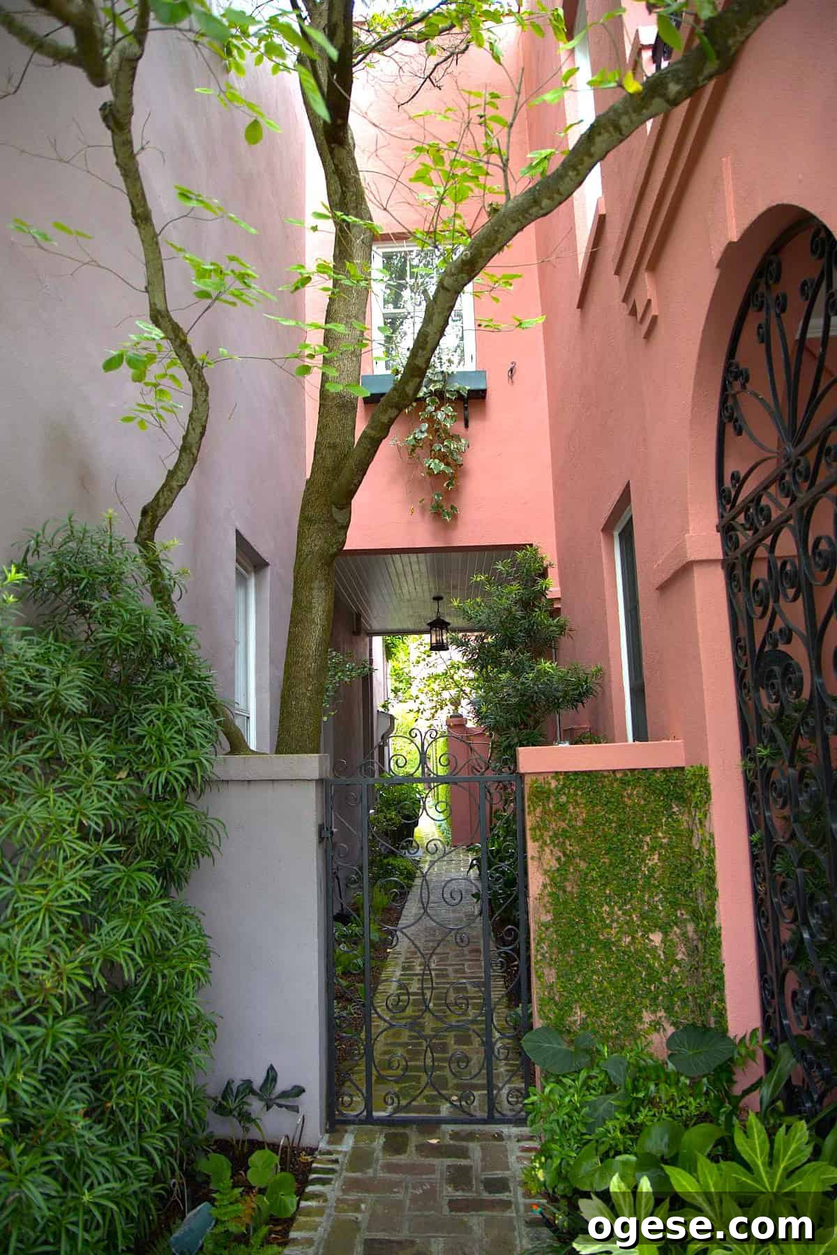 Charleston Travel Guide: Top Attractions, Food & Historic Tours 5 Narrow garden walkway with brick path, wrought iron gate, lush greenery, and pink walls; a tree grows close to the building—a scene straight from a Charleston travel guide.