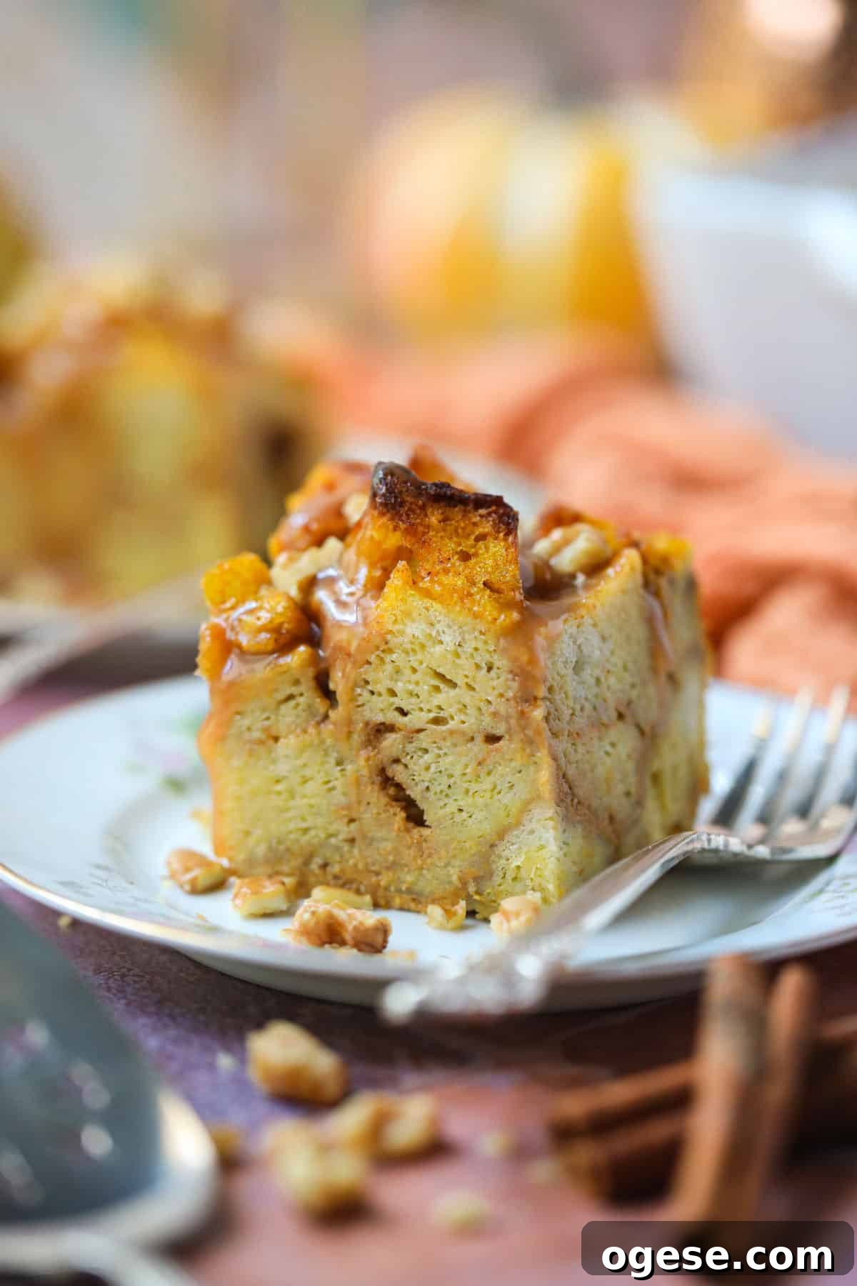 Salted Caramel Pumpkin Bread Pudding Recipe 4 A serving of pumpkin bread pudding with salted caramel sauce and vanilla ice cream on a white dessert plate with a silver fork.