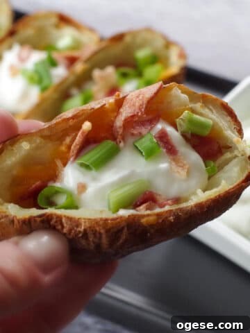 air fryer potato skin being held up over a tray of more air fryer potato skins
