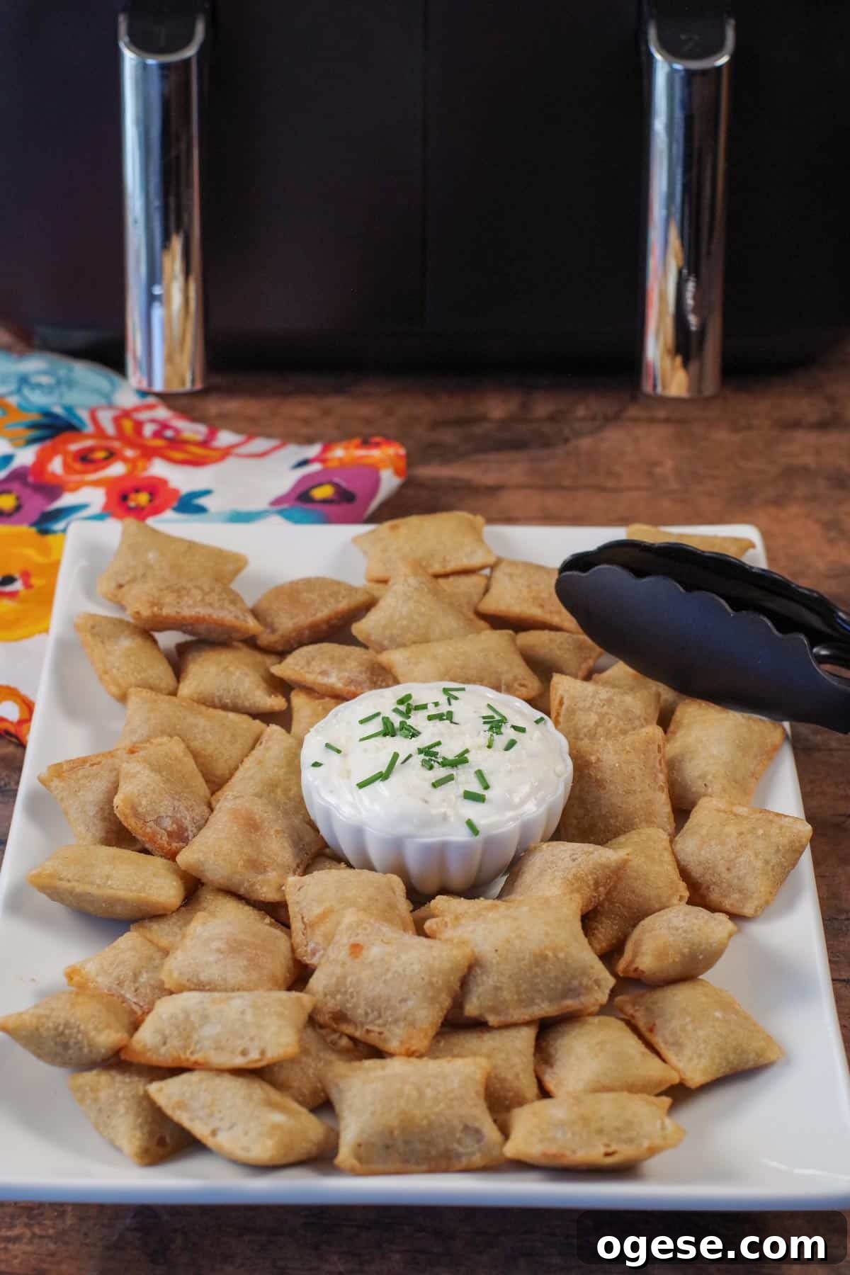 pizza bites on a white serving tray with dip in the middle and tongs on the side, and an air fryer in the background