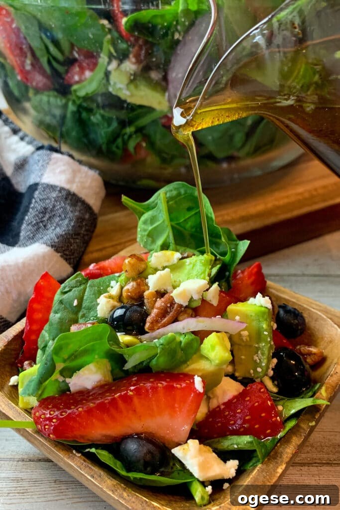 Strawberry spinach salad in a small wooden bowl with balsamic dressing being poured over it.