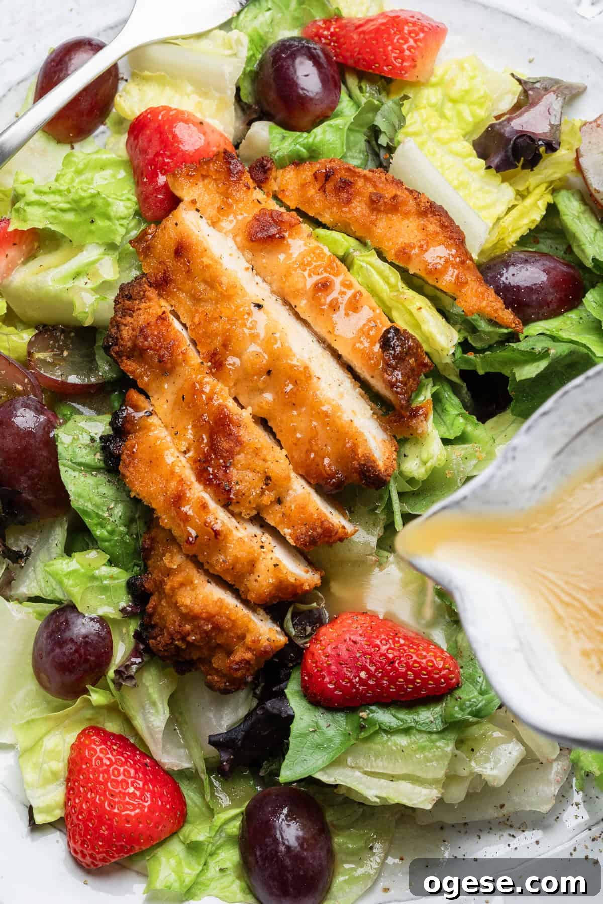 Pouring honey mustard over chicken on a salad.