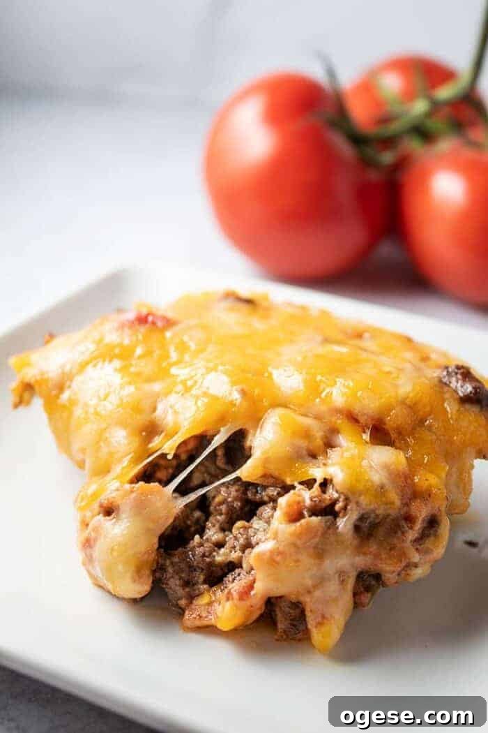 Low-Carb Taco Casserole with Cheesy Cauliflower Crust 2 slice of keto taco casserole on a white plate with tomatoes in background