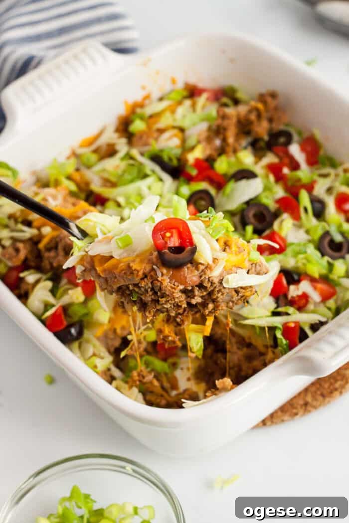 Low-Carb Taco Casserole with Cheesy Cauliflower Crust 11 white casserole dish with spoon scooping out low carb taco casserole piece