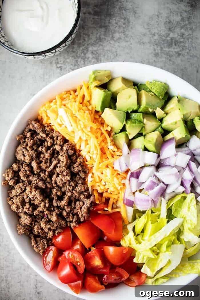 Low-Carb Taco Casserole with Cheesy Cauliflower Crust 12 large white bowl containing keto taco salad next to a small bowl containing sour cream