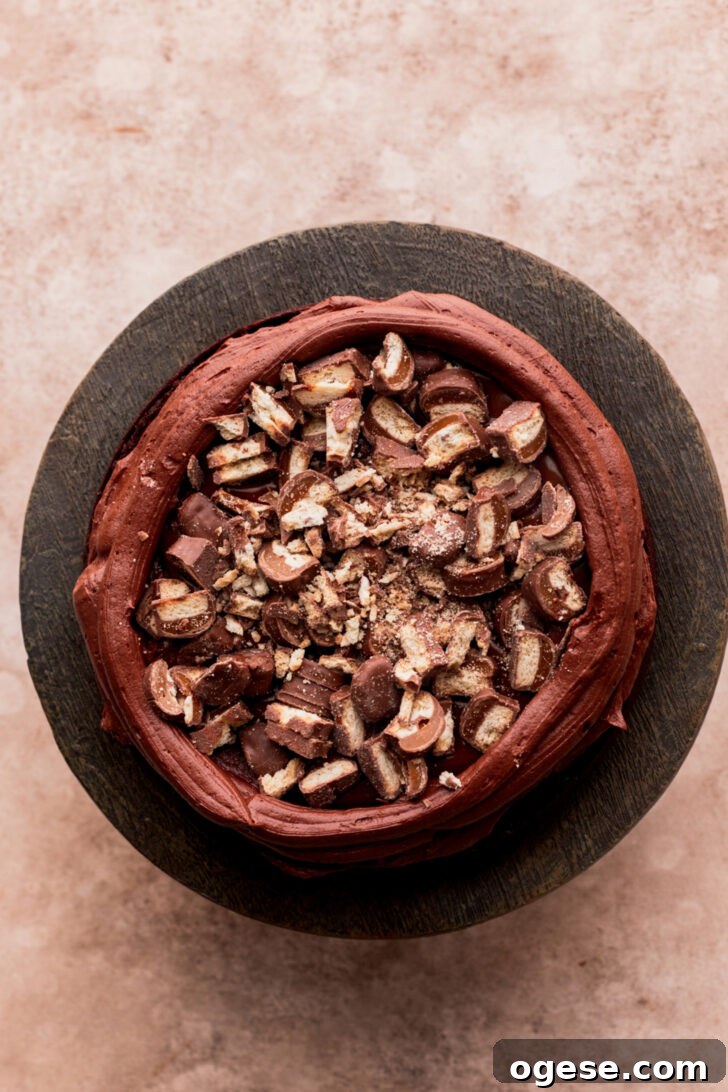 Decadent Twix Bar Cake Recipe with Caramel and Chocolate 8 Chopped twix on top of cake.