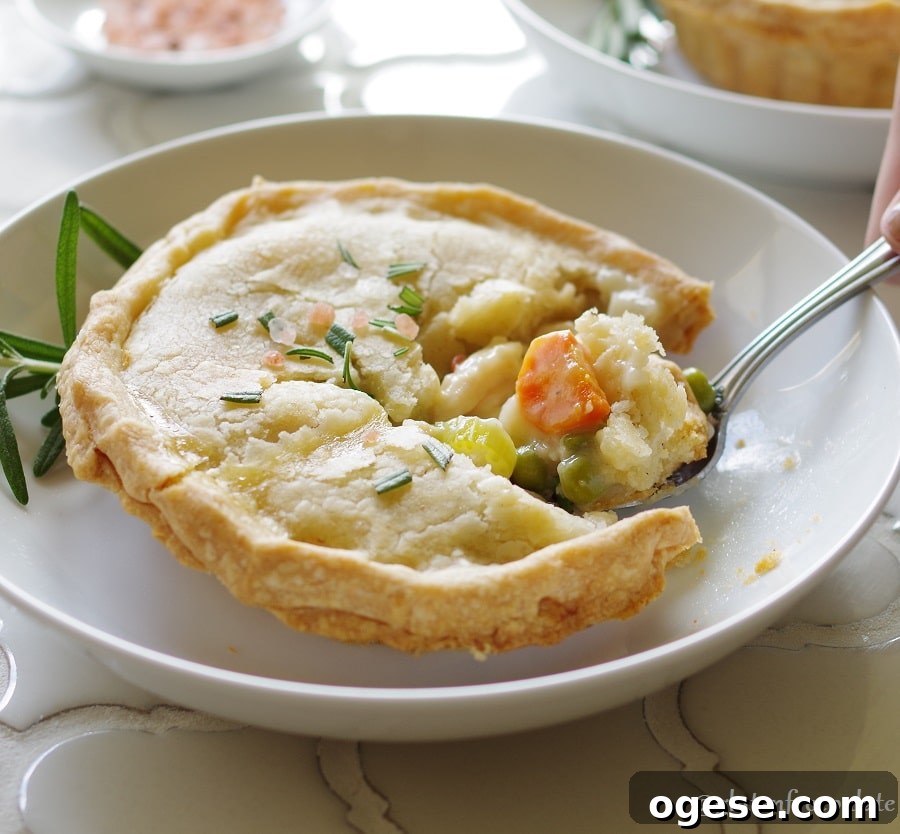 a Gluten-Free Chicken Pot Pie topped with salt and rosemary on a white plate, with a spoon taking a bite out