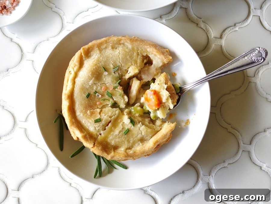 a top down view of a Gluten-Free Chicken Pot Pie topped with salt and rosemary on a white plate, with a spoon taking a bite out