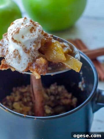 spoon with apple crisp being held up above a black mug
