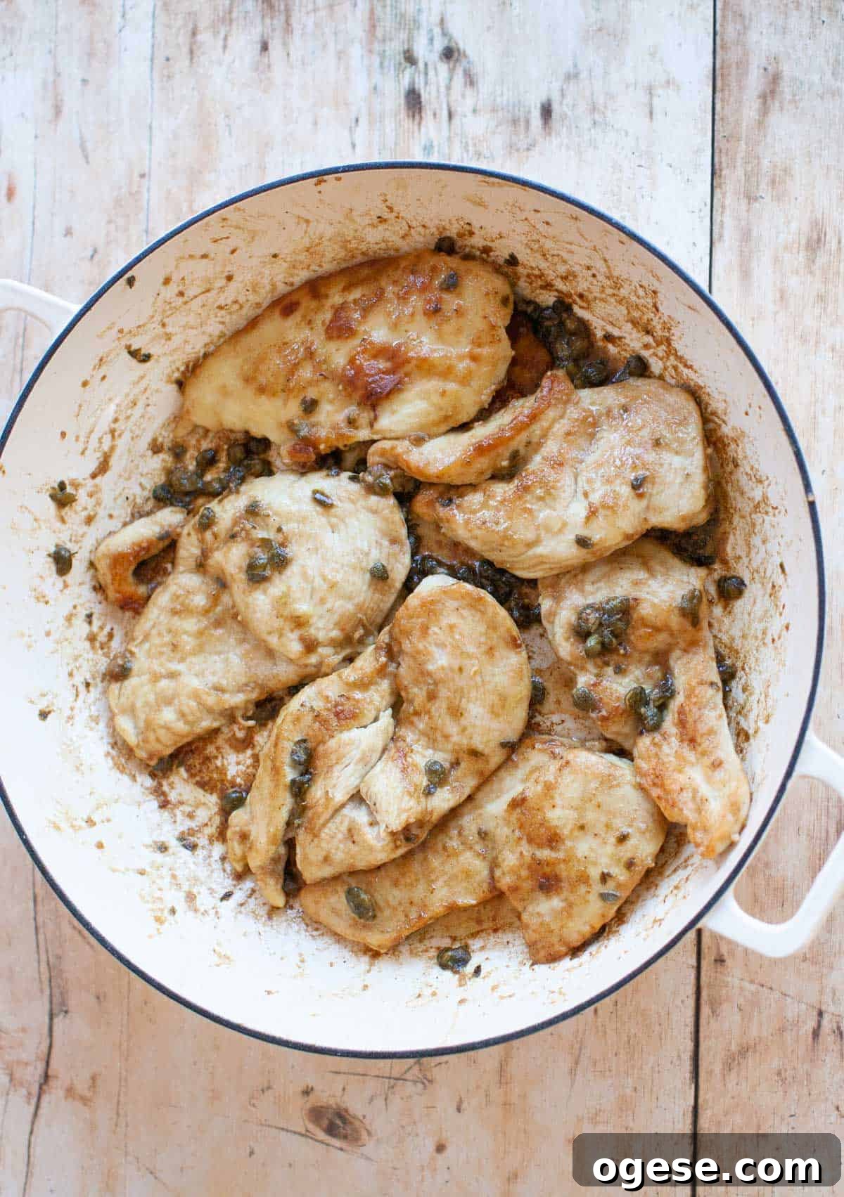 A white pan with cooked chicken piccata in it, sitting on a wooden surface.