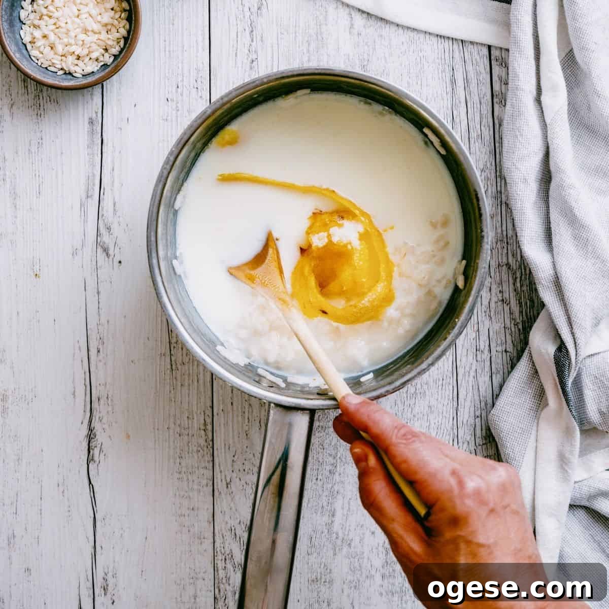 a pot filled with rice, milk and lemon being stirred by a wooden spoon.