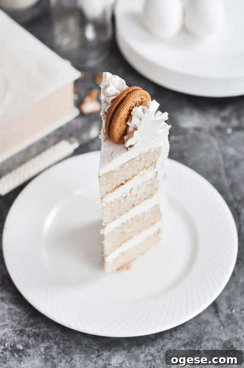 A cake slice standing on a white plate with a buttercream swirl on the top and a golden oreo