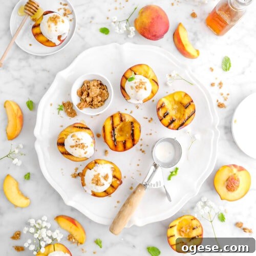 overhead shot of five grilled peaches on white platter with more grilled peaches around, peach slices, and mint leaves