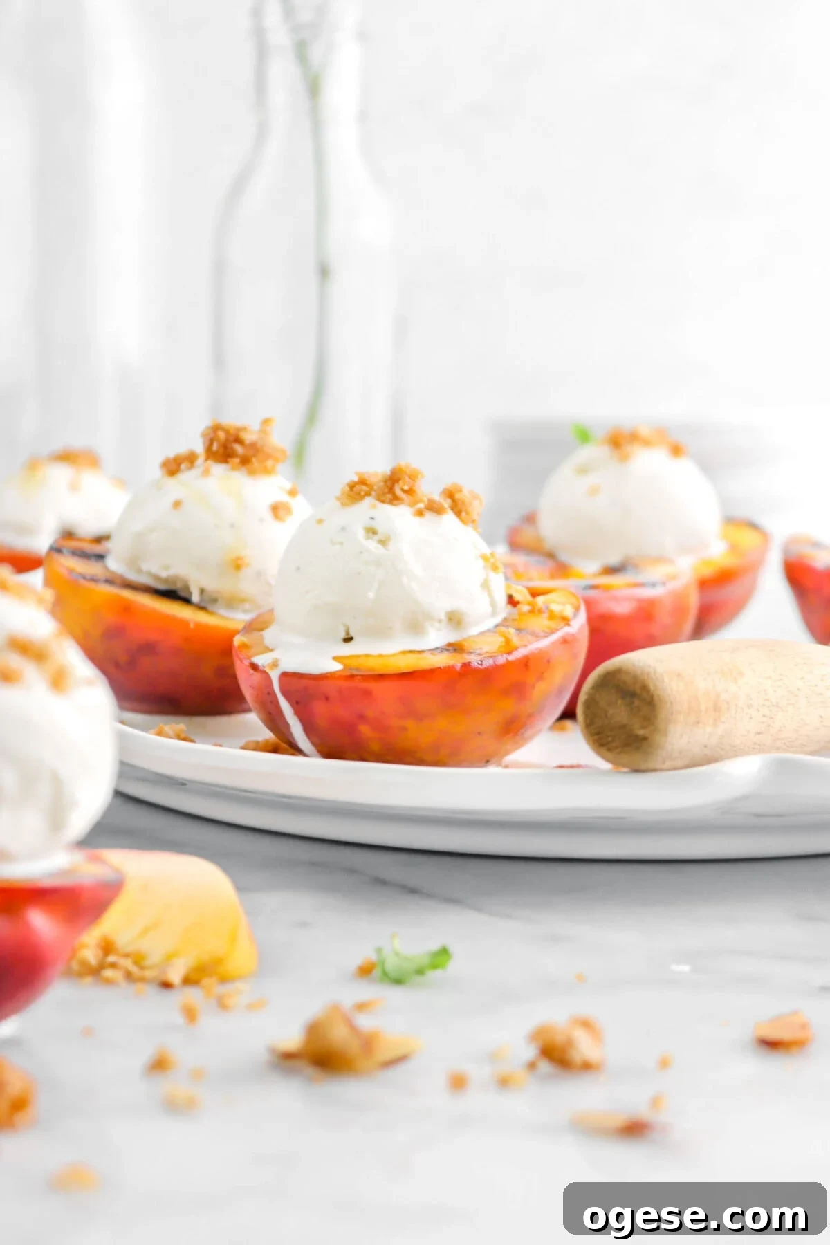front shot of grilled peach on white platter with more peaches behind
