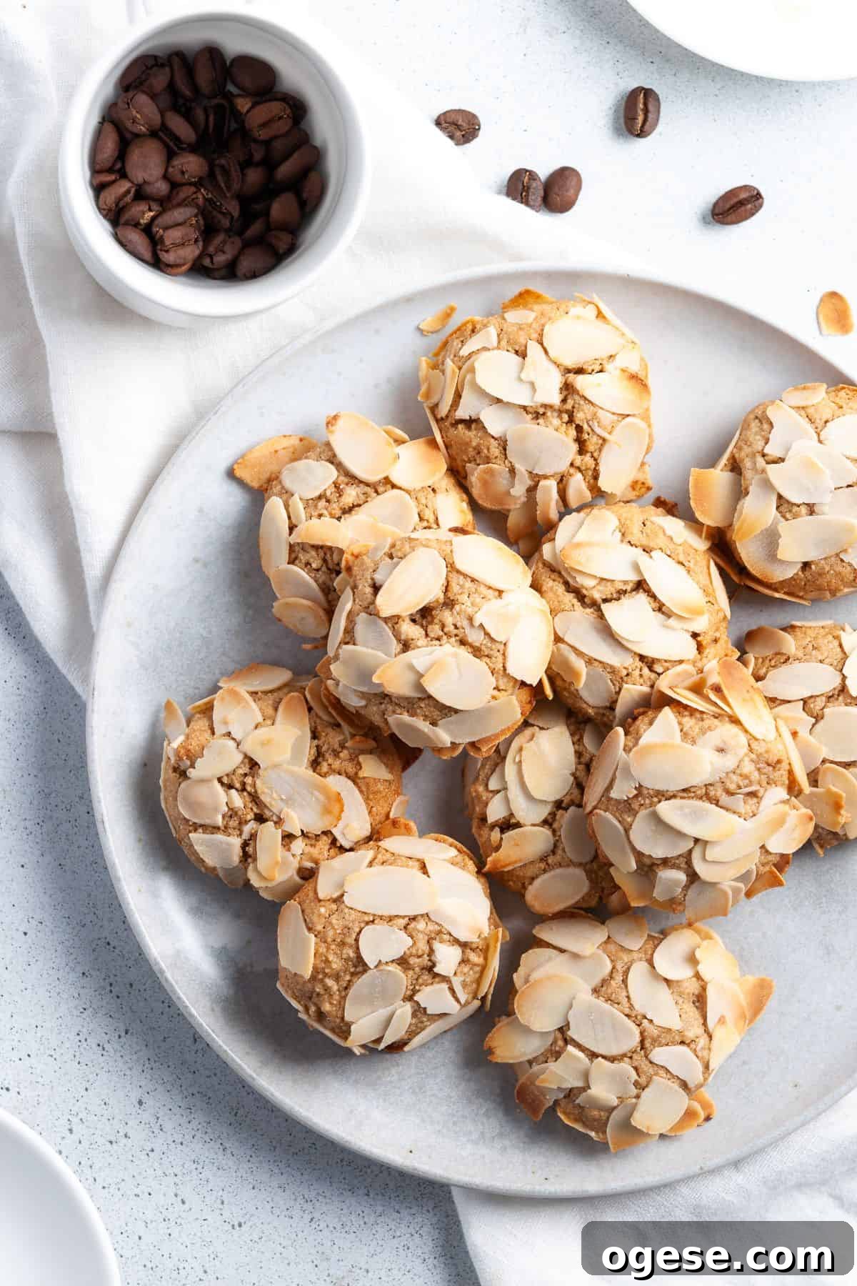 Round plate topped with cookies, sitting on a white cloth with some coffee beans around the edge.