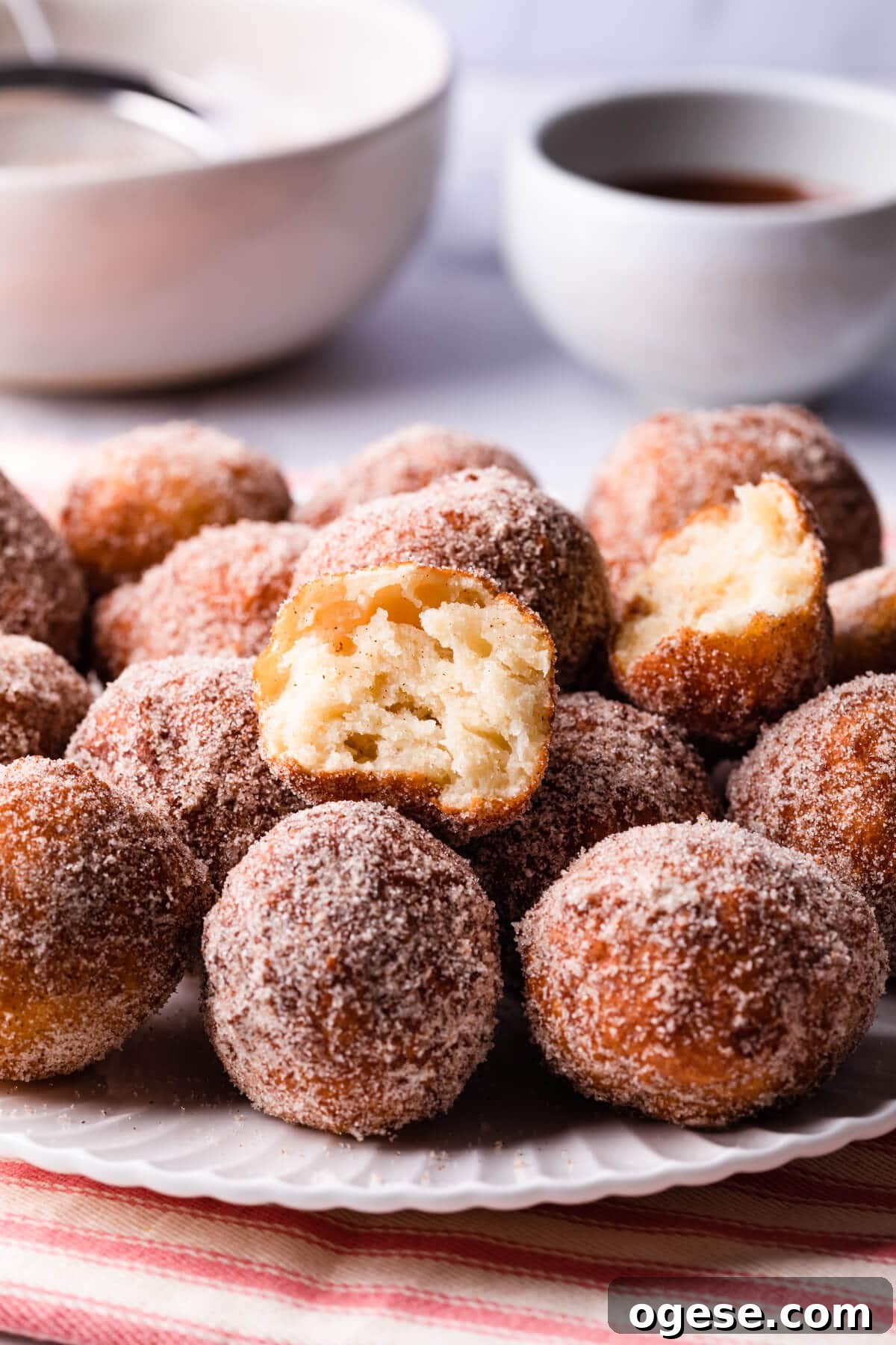 Madeleine-Style Tofu Doughnuts: Light, Protein-Packed Treats 2 tofu donuts on a white plate coated in cinnamon sugar.