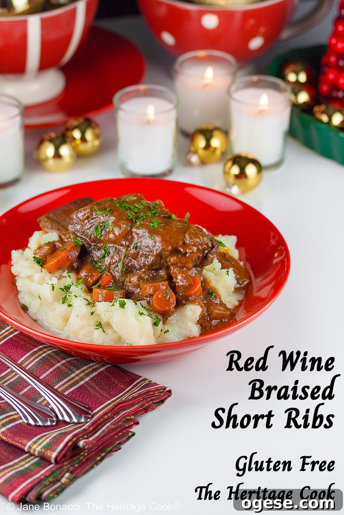 Red Wine-Braised Short Ribs (Gluten-Free) 10 Garlic mashed potatoes lining a red bowl and topped with Red Wine Braised Short Ribs and carrots, in front of festive candles and Christmas decorations with holiday place mats © 2025 Jane Bonacci, The Heritage Cook.
