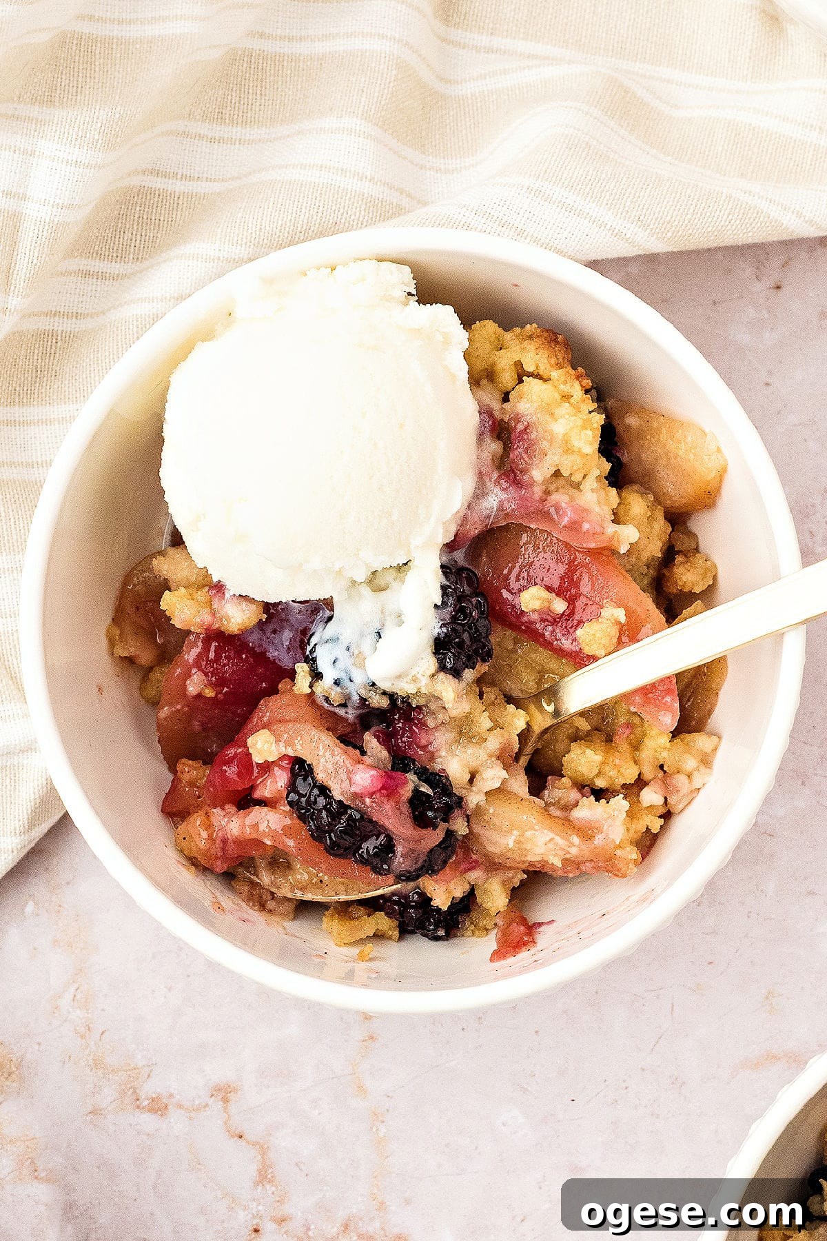 Beige background and white bowl of apple blackberry crumble with ice cream. 