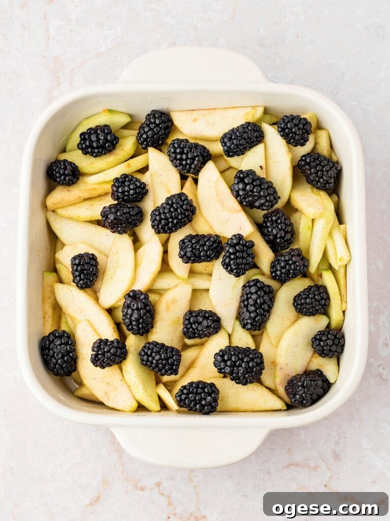 White dish with apple slices and blackberries. White background.