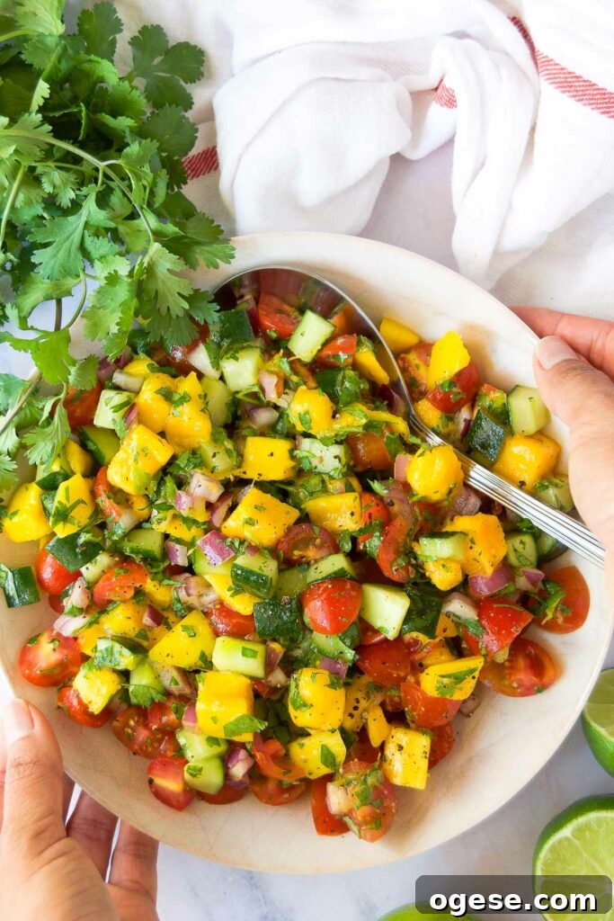 two hands hold a bowl of bright cucumber mango salsa