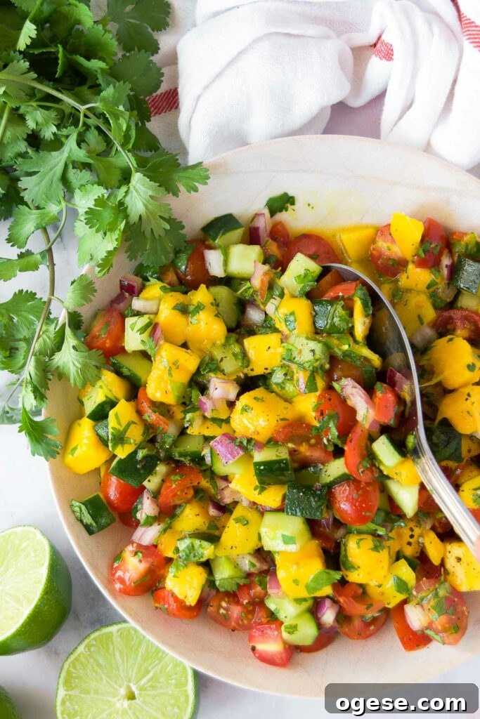 close up of a spoon inside a bowl of cucumber mango salsa