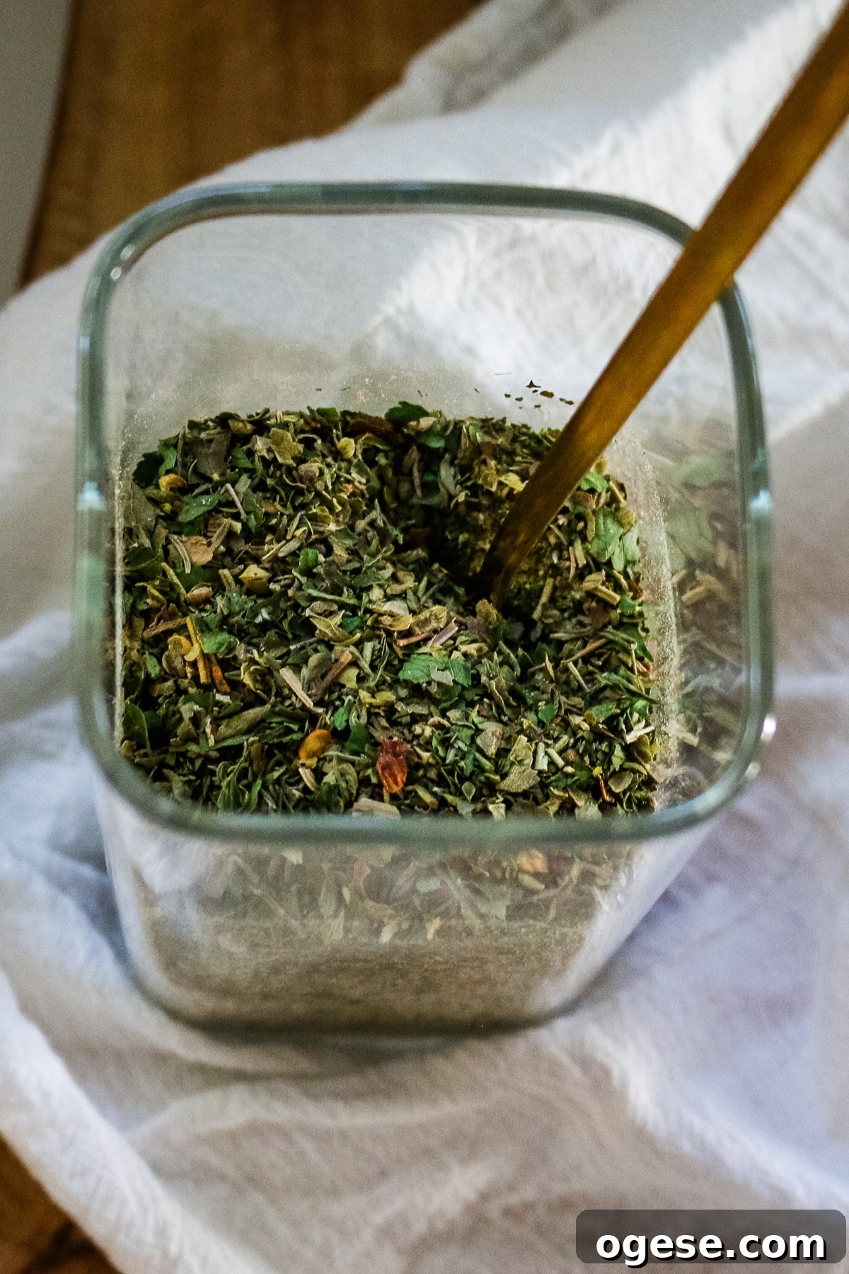 Italian seasoning in a clear jar with a spoon in it.